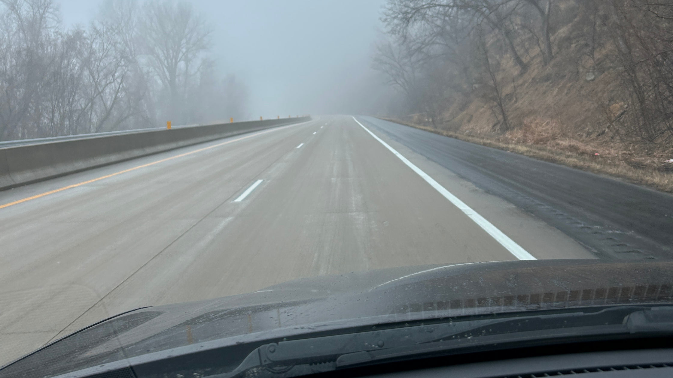 A view through a car windshield of an empty, misty highway surrounded by winter trees, symbolizing finding clarity during moments of uncertainty.