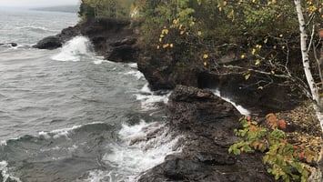 Waves crashing into rock cliffs with trees above, evoking the calming, resonant energy connected to healing sound frequencies.