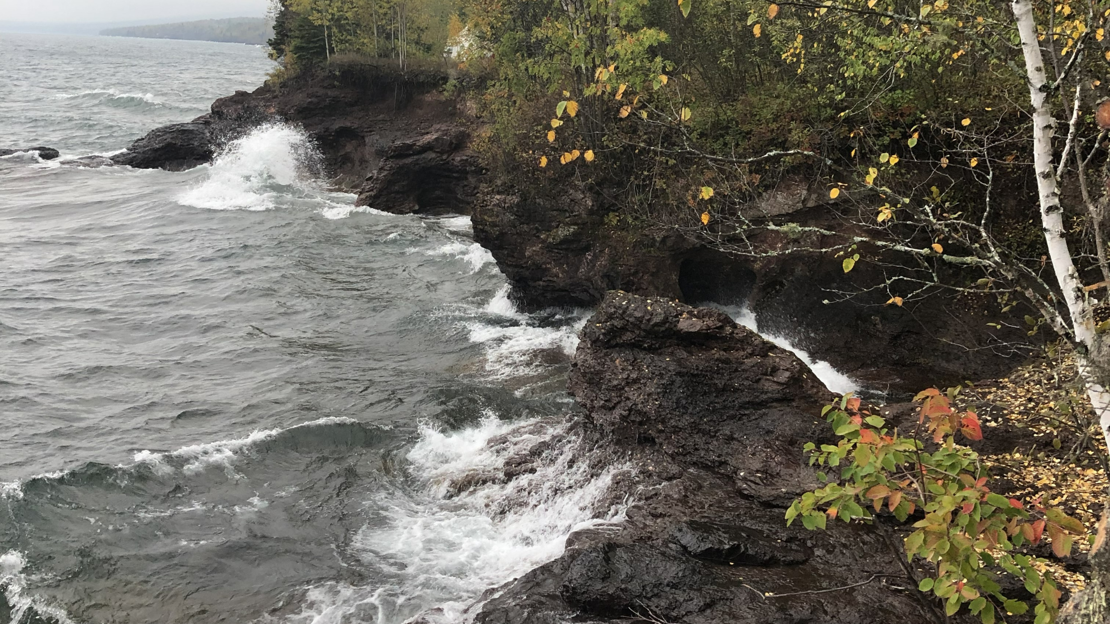 Waves crashing into rock cliffs with trees above, evoking the calming, resonant energy connected to healing sound frequencies.